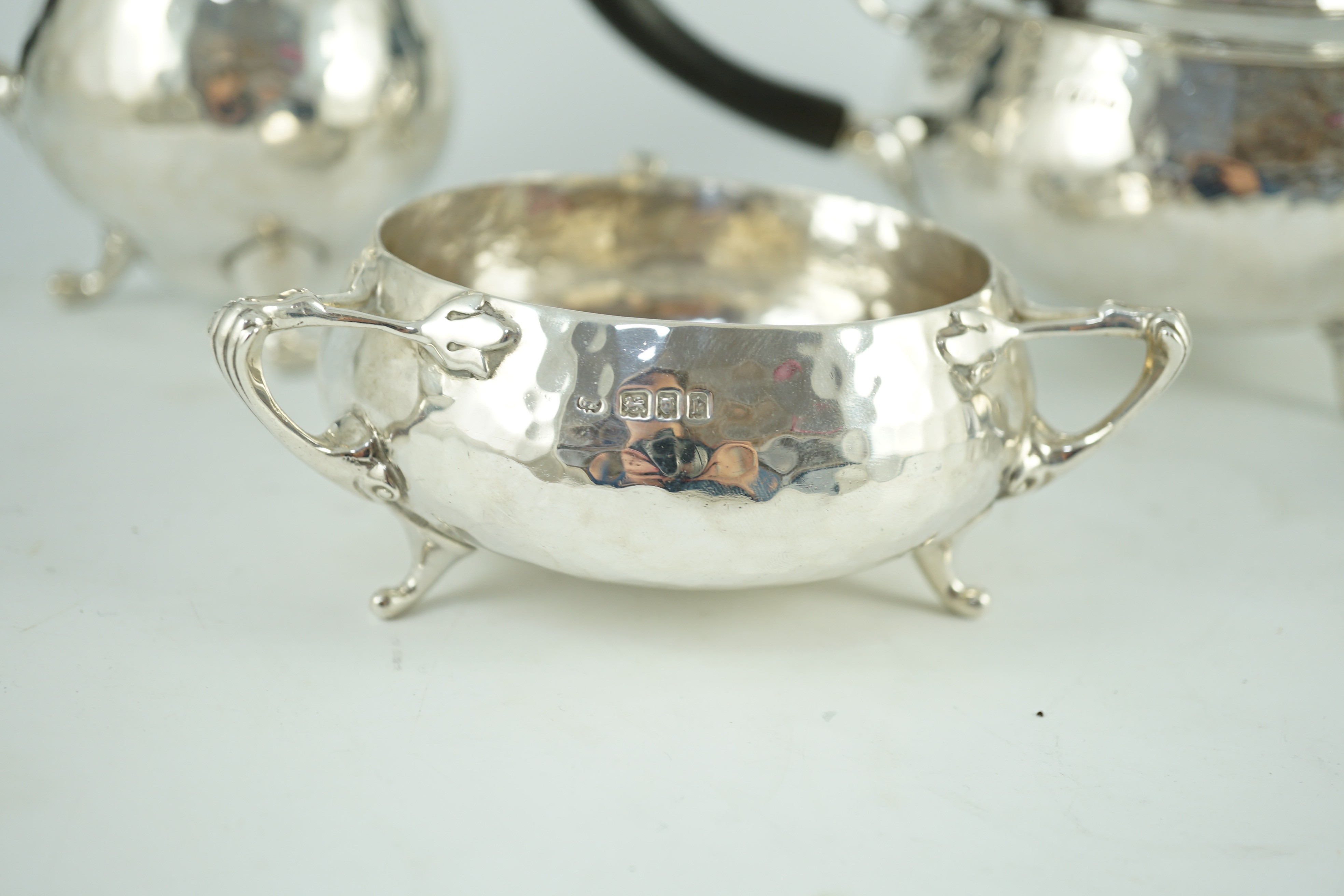 A George V Arts and Crafts three piece planished silver tea set and a similar hot water pot, by Charles Edwards